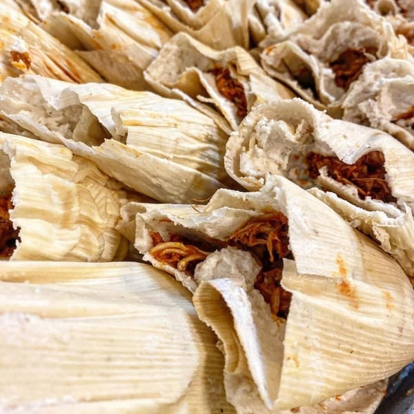 Close-up of many Super Burrito & Taqueria tamales, some with corn husks peeled back to show the filling.